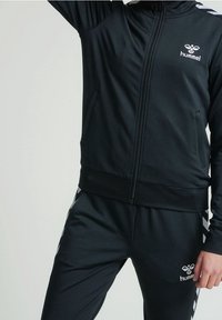 Black athletic tracksuit made of smooth fabric, featuring a zippered jacket with logo and striped accents on pants. Waistband is elastic.