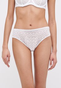 Weiße Spitzenunterwäsche mit einem Blumenmuster, welligen Kanten und einer glatten Textur. Das Design ist tief geschnitten und bietet vollständige Abdeckung.