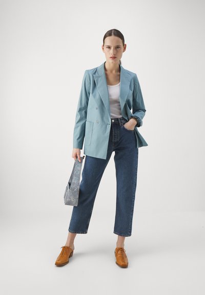 Blazer doppiopetto azzurro chiaro, canottiera bianca, jeans blu a vita alta, scarpe stringate marroni e borsa a tracolla con motivo.