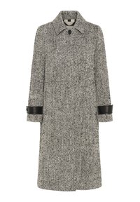 Manteau long à motif chevrons noir et blanc avec des sangles en cuir noir aux poignets et un seul bouton visible au col.