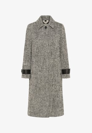 Black and white herringbone patterned long coat with black leather cuff straps and a single visible button at the collar.