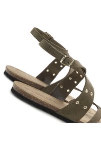 Olivgrüne Wildledersandalen mit mehreren Riemen, Metallnagelakzenten und einer hellbraunen Korkfußbett. schwarze Gummisohle für besseren Halt.