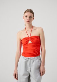 Rød rynket stroppeløs topp med en front cutout og halterneck-design, kombinert med lysegrå bukser med elastisk midje og snor.
