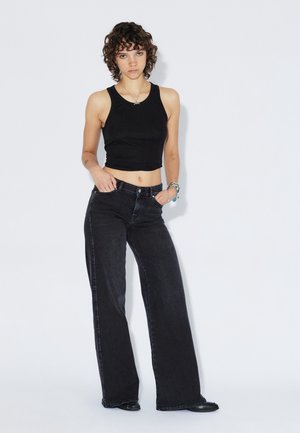 Top nero corto abbinato a jeans neri a gamba larga e vita alta. I jeans presentano un classico design con cinque tasche e una texture sottile.