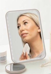 Mirrored makeup mirror with a white frame, illuminated edges, and a round tabletop design; features a person using a cotton pad.