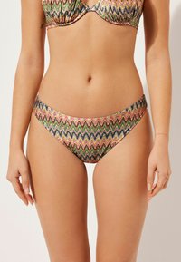 Flerfärgad bikiniunderdel med ett zigzag-mönster i rosa, grönt och svart. Den har en låg skärning och en mjuk, glänsande tygtextur.