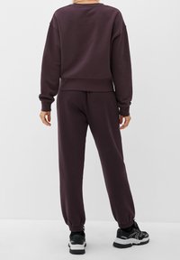 Felpa di cotone viola scuro con polsini a coste e pantaloni da jogging abbinati. Scarpe da ginnastica nere con dettagli bianchi. Design semplice e comodo, vestibilità rilassata.