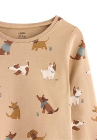 Beige langærmet skjorte med et tryk af hunde i forskellige farver over hele stoffet. Rund halsudskæring, blød tekstur, legende hundeillustrationer og græsdetaljer.