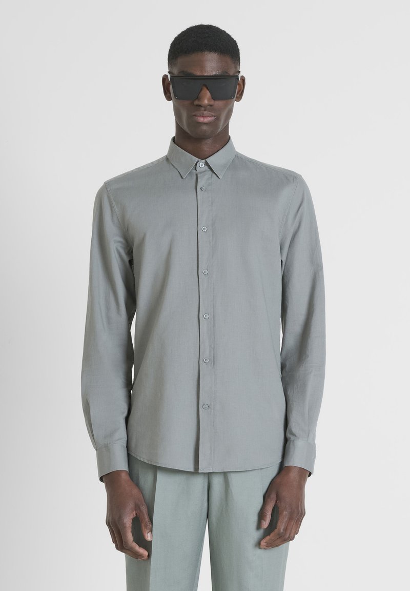 Camisa de manga larga gris claro con cuello tipo button-down, textura suave y corte recto, combinada con pantalones grises claros a juego.
