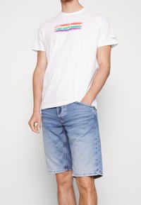 Camiseta blanca con un logo multicolor de "Pepe Jeans London", combinada con shorts de mezclilla azul claro. Ambos artículos son casuales y ajustados.