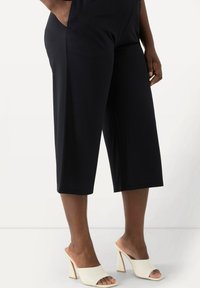 Svarta culotte-byxor i mjuk väv, med sidofickor och vid passform. Bärs med vita öppna klackar med blockklack.