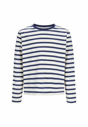 Smilende dreng stående, iført en hvid og navy stribet langærmet skjorte, løse lyseblå jeans og beige sko på hvid baggrund.