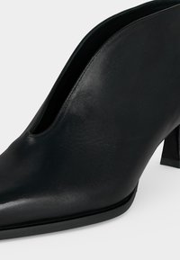 Chaussure à talon haut pour femme en cuir noir à bout pointu, finition lisse et talon bloc sur fond blanc.
