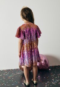 Robe à paillettes avec de courtes manches volantes, arborant des nuances multicolores de rose, violet et or. Texture brillante, coupe au genou.