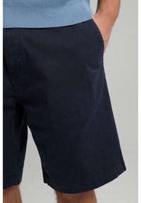 Navy cotton shorts with a relaxed fit, featuring side pockets and hemmed cuffs, shown with a light blue knitted sweater.