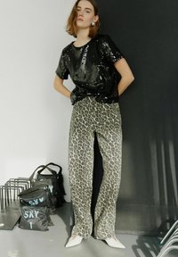 Top en sequins noir à manches courtes, associé à un pantalon large léopard gris clair et des chaussures blanches à bout pointu.