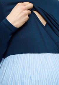 Μπλε ναυτικό τοπ με μακριά μανίκια που διαθέτει σκούρο γαλάζιο ριγέ, ελαφρώς πιεσμένο κάτω μέρος. Ένα πλαϊνό άνοιγμα προσφέρει εύκολη πρόσβαση. Μαλακή υφή υφάσματος.