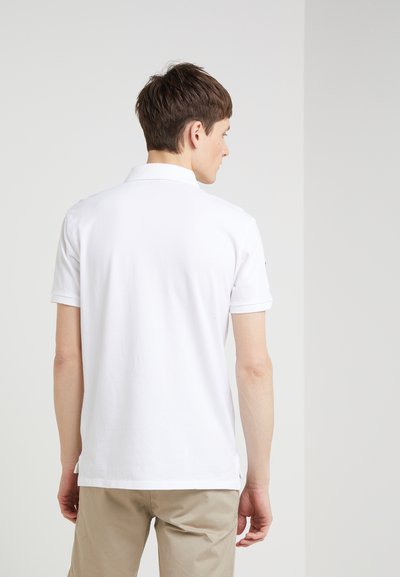 Biała koszulka polo wykonana z bawełny, z klasycznym kołnierzykiem, krótkimi rękawami i prostym dołem z bocznymi rozcięciami. Minimalistyczny design.