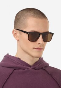 Akiniai nuo saulės su juodu ir vėžlio rago spalvos rėmeliu, stačiakampio formos, su rudomis lęšiais. Komplekte liekni šonai su subtiliu prekės ženklo elementu.