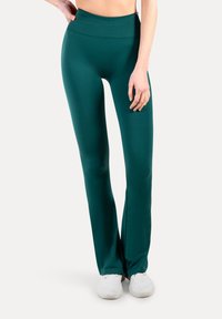 Ciemnoturkusowe legginsy z wysokim pasem, wykonane z elastycznego materiału. Mają dopasowany fason zwężany ku dołowi oraz subtelne rozcięcia przy kostkach.