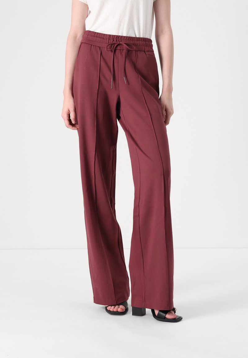 Loose-fitting, burgundy trousers with an elastic drawstring waist, front pleats, and wide legs, made from soft, smooth fabric.