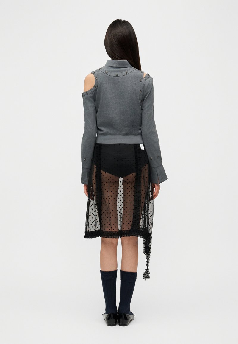 Grå kold-shoulder bluse med nitteaccenter, lagdelt over en gennemsigtig sort polkaprikket nederdel. Sorte sokker og sko fuldender outfittet.