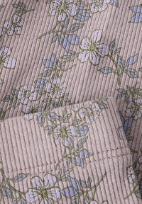Tissu côtelé en rose doux avec un motif floral en bleu clair et vert. Présente des fleurs délicates et des feuilles, avec des détails de couture visibles.
