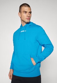 Felpa blu brillante realizzata in morbido tessuto, con tasca frontale, cappuccio regolabile con stringhe e testo del logo bianco sul petto.