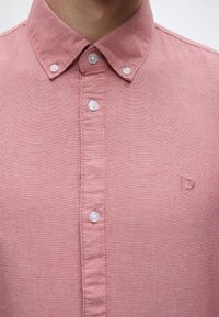 Πουκάμισο με κοντά μανίκια σε ανοιχτό ροζ χρώμα, κατασκευασμένο από υφασμένο ύφασμα, με λευκά κουμπιά και κεντημένο λογότυπο στο στήθος.