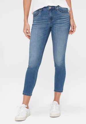 High-rise blue denim jeans with slim fit, featuring five-pocket design and subtle fading. Paired with white sneakers for contrast.