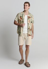 Korte mouwen, multikleurig shirt met abstracte patronen, gecombineerd met beige shorts en bruine sandalen met een gesp detail.