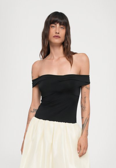 Sort off-shoulder top lavet af strækbart stof, parret med en voluminøs hvid nederdel. Har smocket talje og elegante design detaljer.