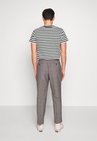 Pruhované zeleno-bílé tričko v kombinaci se šedými kostkovanými kalhotami, které mají dvě zadní kapsy a uvolněný střih. Hladká textura látky.