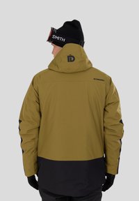 Olivově zelená bunda s černými akcenty, voděodolný materiál, nastavitelná kapuce a logo na zadní straně. Texturovaná tkanina s kontrastními barvami.