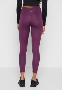Fioletowe legginsy z wysokim stanem, charakteryzujące się gładką fakturą, dopasowanym krojem i subtelnym logo na pasie, połączone z czarnymi butami sportowymi.