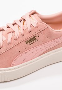 Baskets Puma en suède rose avec lacets assortis, détail de rayure rose clair, logo doré et semelle en caoutchouc blanc.