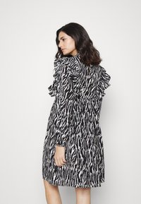 Vestido preto e branco com padrão, mangas longas, detalhes franzidos nas ombreiras e uma silhueta evasê, visto de costas.