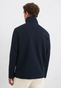 Navyblauwe fleece pullover met een hoge kraag, lange mouwen en een rechte zoom. Heeft een gestructureerde stof en een discreet logo op de mouw.