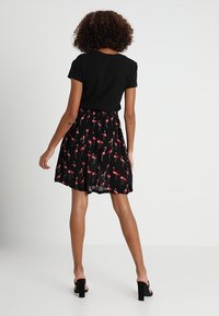 T-shirt noir associé à une jupe légère et évasée ornée d'un imprimé flamant rose sur fond noir. Sandales à talons.