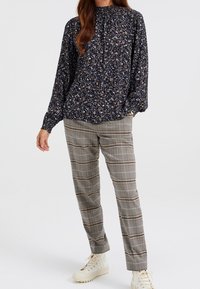 Marinblommig blus med rynkad halsringning och lång ärm, i kombination med rutiga byxor i nyanser av beige, svart och grått. Vita sneakers.