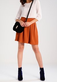 Blouse blanche texturée ; jupe orange évasée ; sac bandoulière noir avec des détails dorés ; bottines bleu marine. Design simple et élégant.