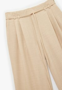 Pantalons beiges taille haute avec plis et une ceinture en tissu. Matière légère et texturée, avec une finition lisse et sans motifs visibles.