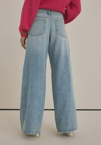 Jeans a gamba larga in denim azzurro chiaro, con vita alta, due tasche posteriori e orlo sfilacciato con una finitura leggermente testurizzata.