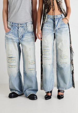 Jeans en denim délavé bleu clair avec des jambes larges et des accents effilochés. Une paire a une coupe décontractée, renforçant l'esthétique casual.