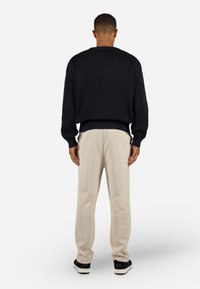 Mørkeblå ribbestrikket sweater med lange ærmer, parret med cremefarvede bukser. Sorte sneakers fuldender outfittet. Set fra bagsiden.