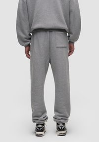 Šedé tepláky s uvolněným střihem, s zadní kapsou a žebrovanými lemy. Nosí se s černobílými teniskami. Měkká textura.