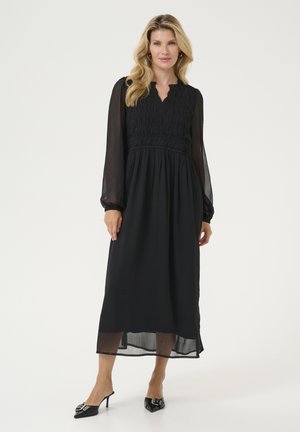 Black maxi dress with a smocked bodice, long sheer sleeves, and a V-neckline. Flows loosely with a knee-length lining and textured fabric.