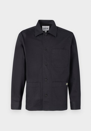 Črna bombažna jakna z gumbi, ovratnikom, dvema sprednjima žepoma in majhnim logotipom na desnem žepu. Minimalističen dizajn.