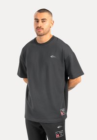 Camiseta de manga corta en gris oscuro fabricada en tejido suave, con un escote redondo y un pequeño logo en el pecho. Incluye una etiqueta en el dobladillo.