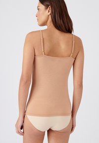 Top in beige con spalline regolabili, design senza cuciture e silhouette aderente, abbinato a biancheria intima beige chiaro. Tessuto di consistenza liscia.